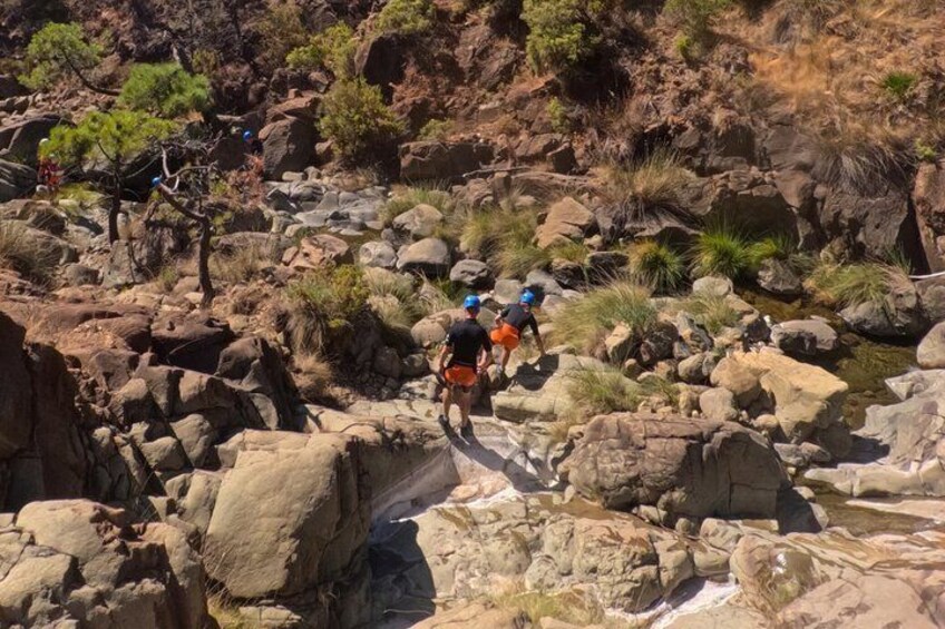 A group of hikers navigating a rocky terrain with large boulders and sparse vegetation. 5