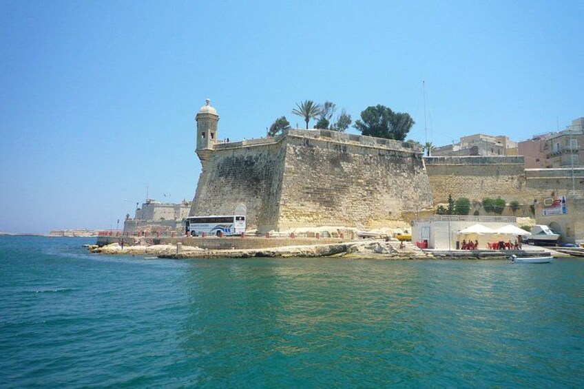Una fortificazione costiera con un faro, un autobus e una piccola barca ormeggiata nelle vicinanze. 1