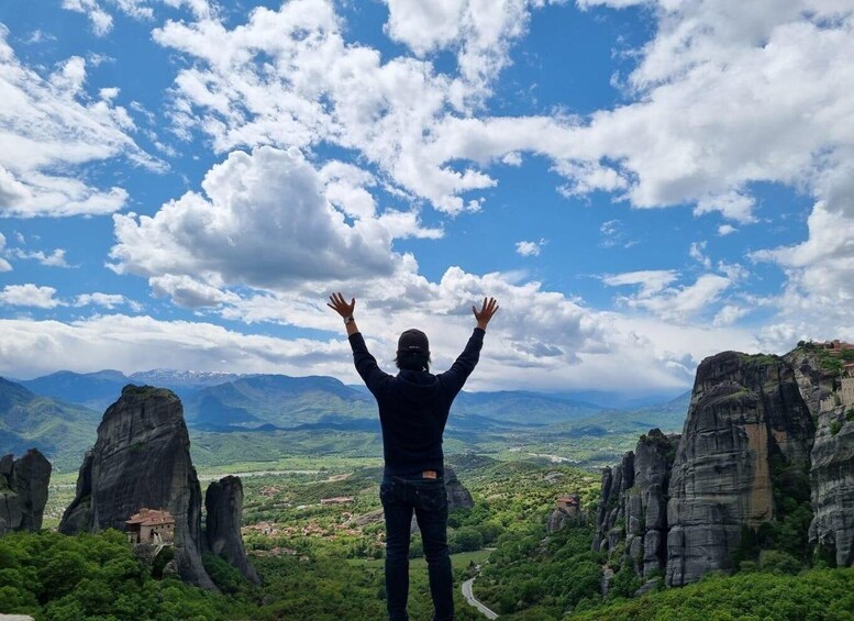 Una persona de pie con los brazos levantados, contemplando un paisaje montañoso con formaciones rocosas y un pueblo abajo. 4