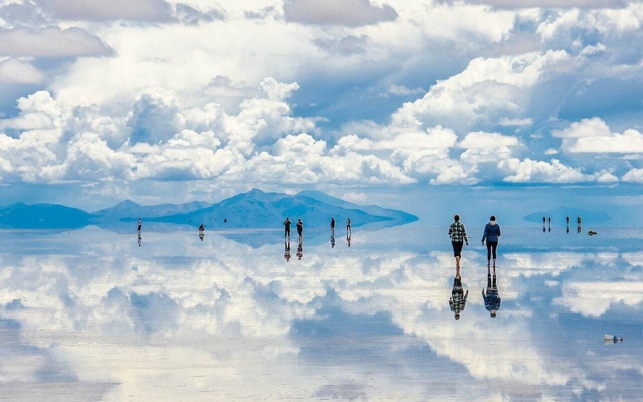 A group of people walking on a reflective salt flat with mountains in the background. 4