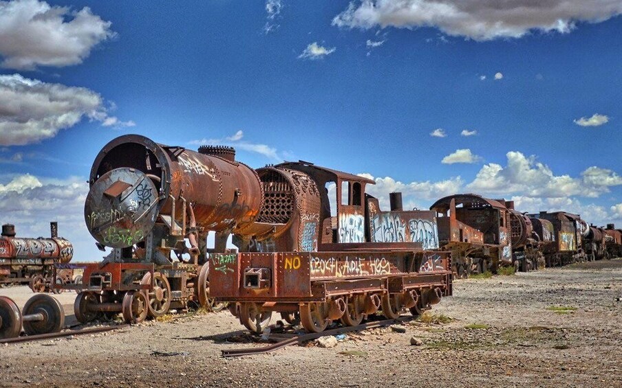 A rusted train with graffiti, tracks, and a clear blue sky. 2