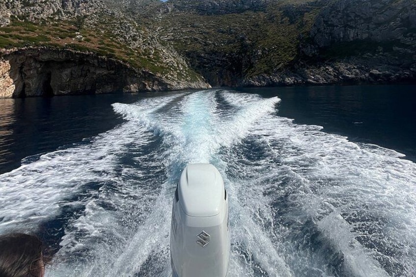 A boat moving through water with waves created behind it, surrounded by rocky cliffs and greenery. 3
