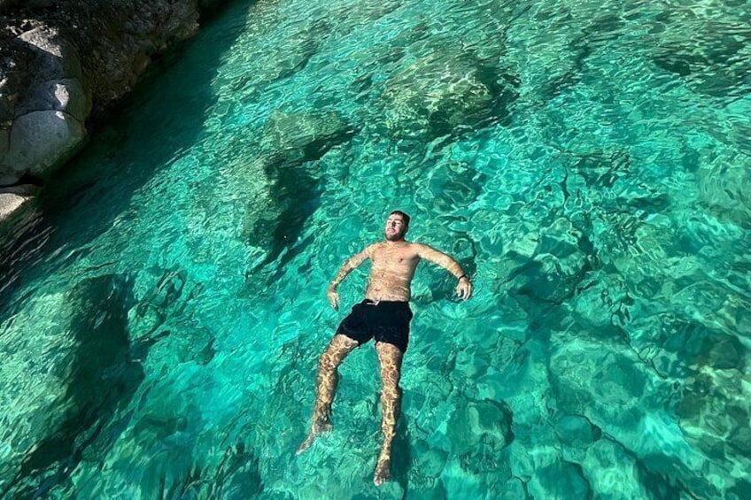A person floating in clear turquoise water with rocks on the side. 2