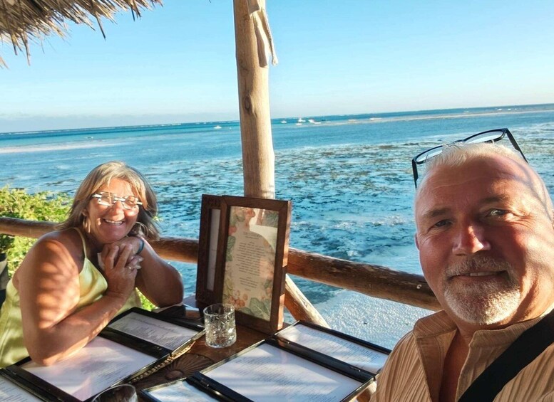 Et træbord med en menu, et glas vand og et indrammet billede i en restaurant ved havet. 5