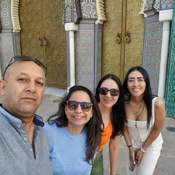 A group of people posing in front of a building with ornate, patterned doors and columns. 1