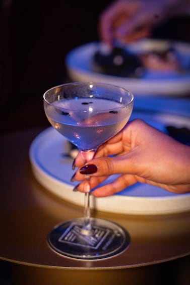 A hand holding a martini glass with a blue drink. 2