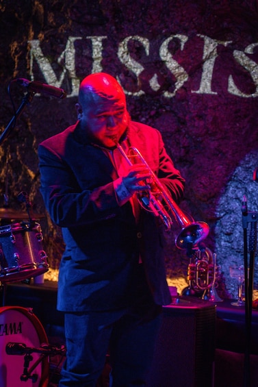 A person playing a trumpet on stage with a drum set in the background. 3