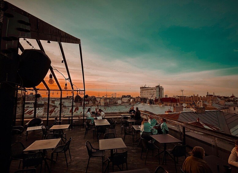A rooftop terrace with tables and chairs, overlooking a cityscape during sunset. 1