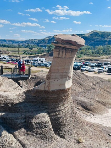A large rock formation with a flat top, surrounded by a parking lot and a scenic landscape with hills and trees. 1