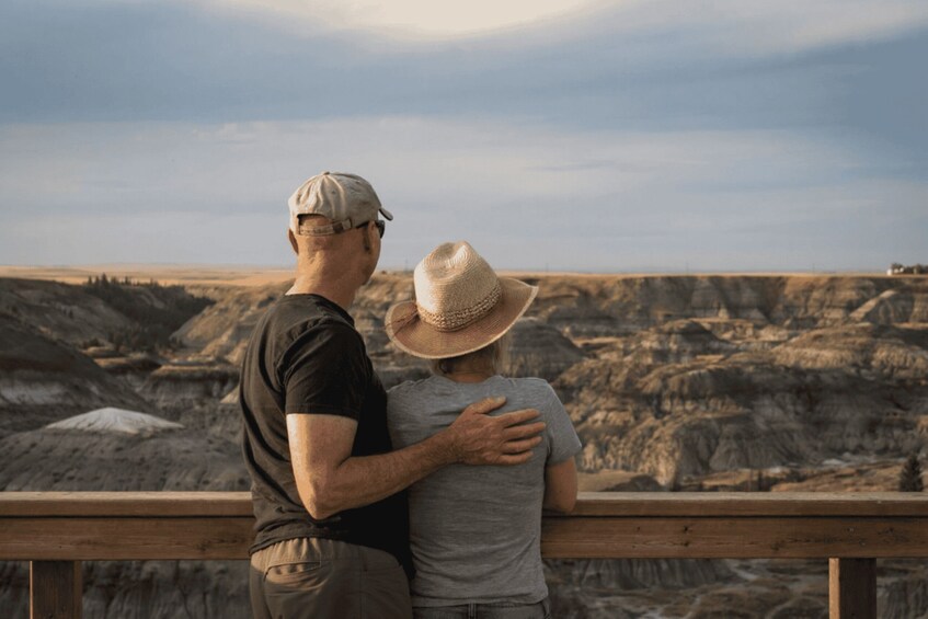 A man and a child standing on a wooden railing, overlooking a vast, rugged landscape with layered rock formations. 2