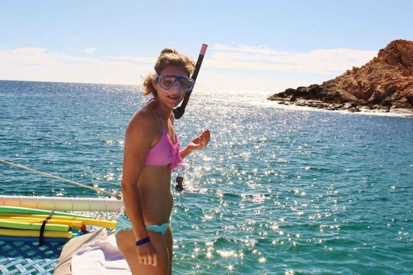 Una persona haciendo snorkel en el océano, con un barco y una costa rocosa al fondo. 2
