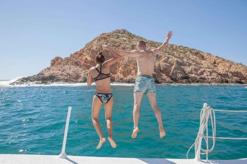 Dos personas saltando desde un bote al mar, con una isla rocosa de fondo. 1