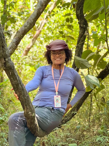 A person sitting on a tree branch in a forested area. 4