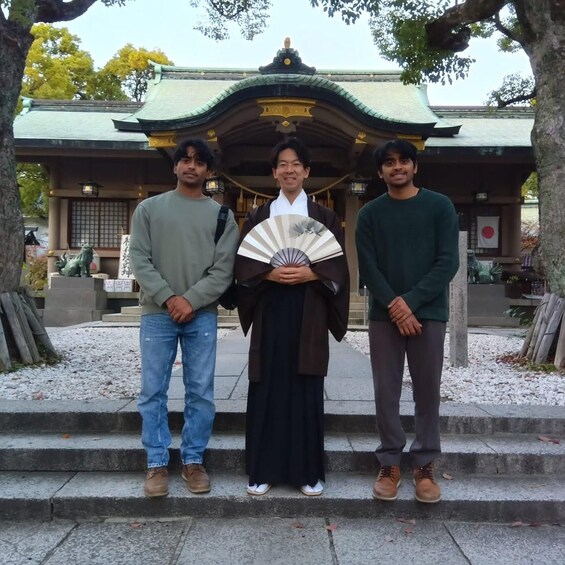 Three people standing in front of a traditional Japanese building with a green roof and a statue of a lion. 2