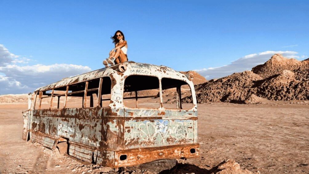 A rusted bus with graffiti, a desert landscape, and rocky hills in the background. 1