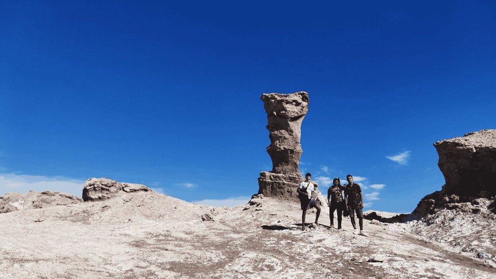 A group of people standing near a tall, isolated rock formation in a desert landscape. 2