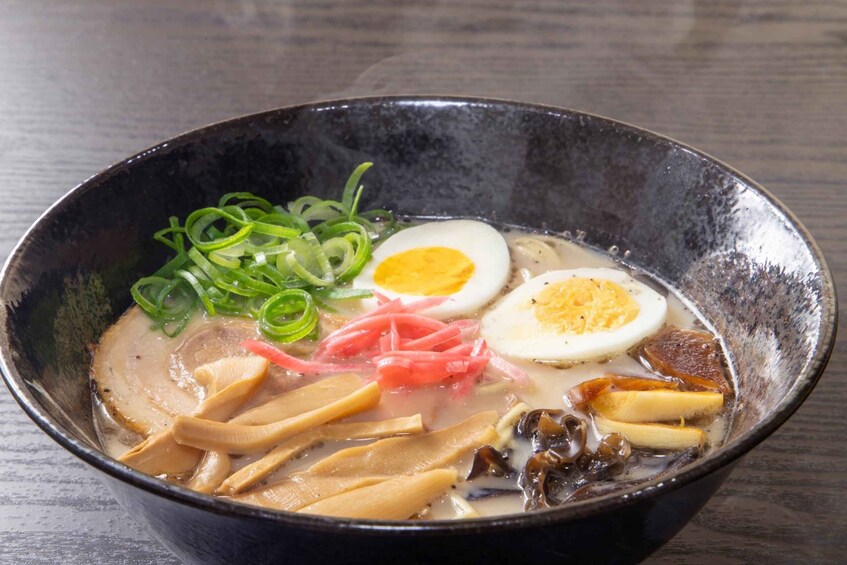 A bowl of ramen with sliced pork, green onions, a soft-boiled egg, and mushrooms. 1