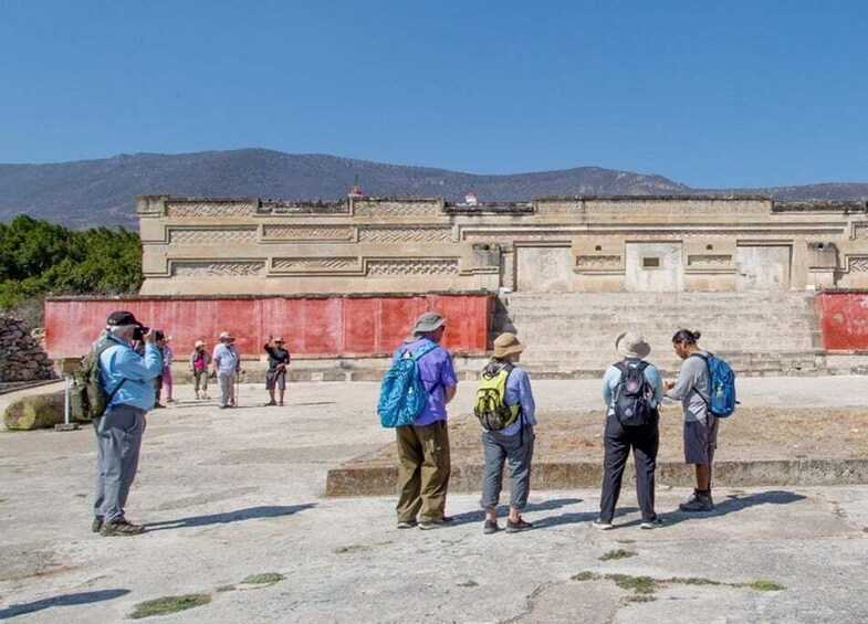 A group of hikers standing in front of a historical building with a mountainous backdrop. 5