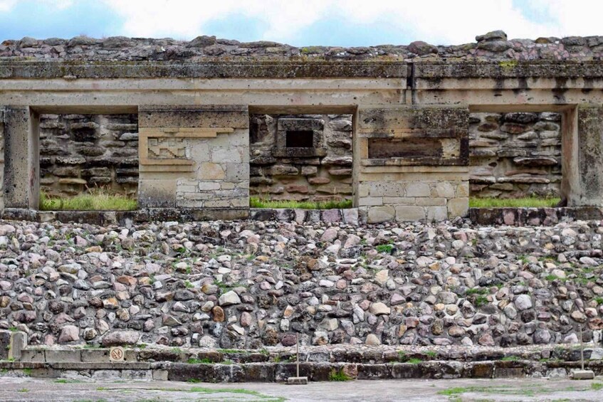 A stone structure with three doorways and a stone wall. 4