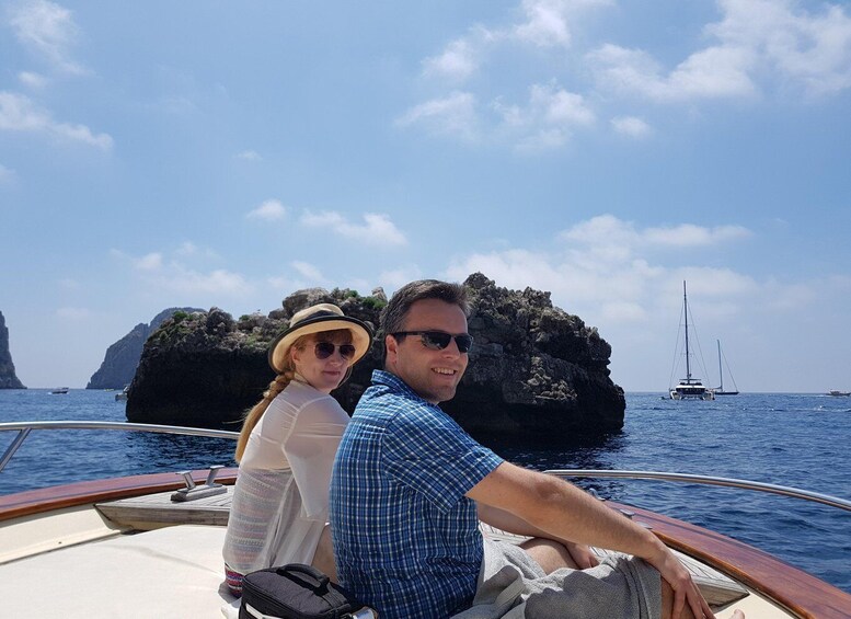 Un couple à bord d’un bateau, avec des falaises rocheuses et des voiliers en arrière-plan. 4