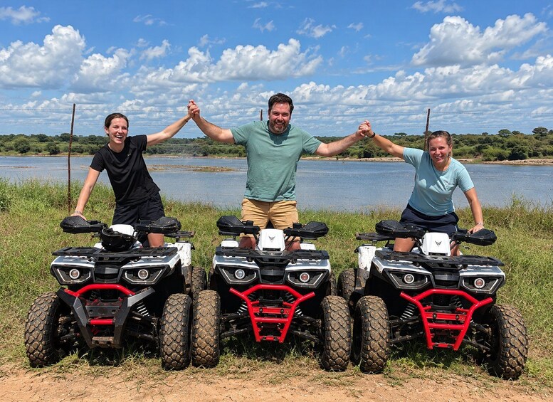 Three people on all-terrain vehicles (ATVs) with a lake and trees in the background. 1
