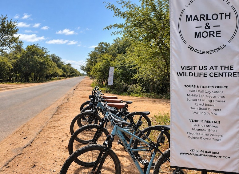 A signboard for Marlooth & More vehicle rentals and tours, with bicycles parked beside a dirt road. 3