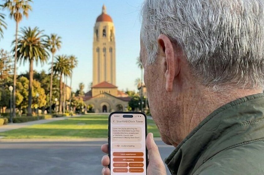 A person holding a smartphone with a Stanford Clock Tower app open, with the tower in the background. 1