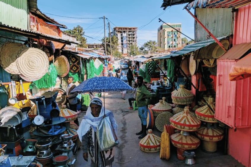 A bustling market street with vendors selling colorful goods, including large woven baskets and metal containers. 3