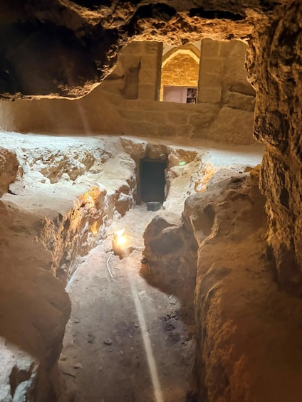 A cave with a person standing in a central chamber, a small light source on the ground, and a doorway at the far end. 4