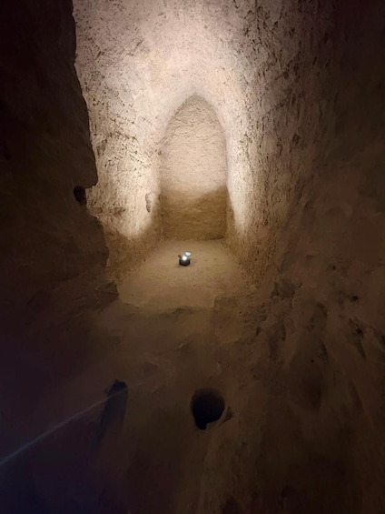 A narrow, arched cave passage with a light source at the end. 3