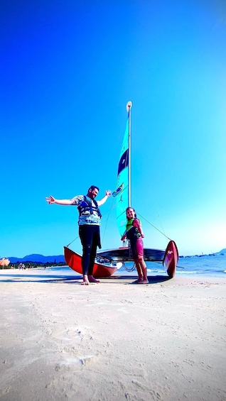 Two people standing on a beach with a sailboat. 2