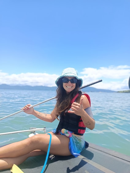 A person sitting on a boat, holding a fishing rod, with a clear sky and calm water in the background. 4