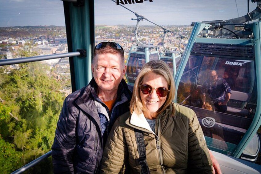 A person in a green jacket and another in a black jacket on a cable car with a cityscape in the background. 3
