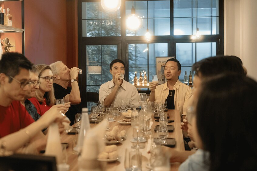 A group of people sitting around a table with wine glasses and bottles, in a room with large windows and hanging lights. 3