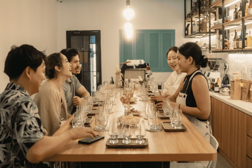 A group of people seated around a long wooden table with wine glasses and bottles. 1
