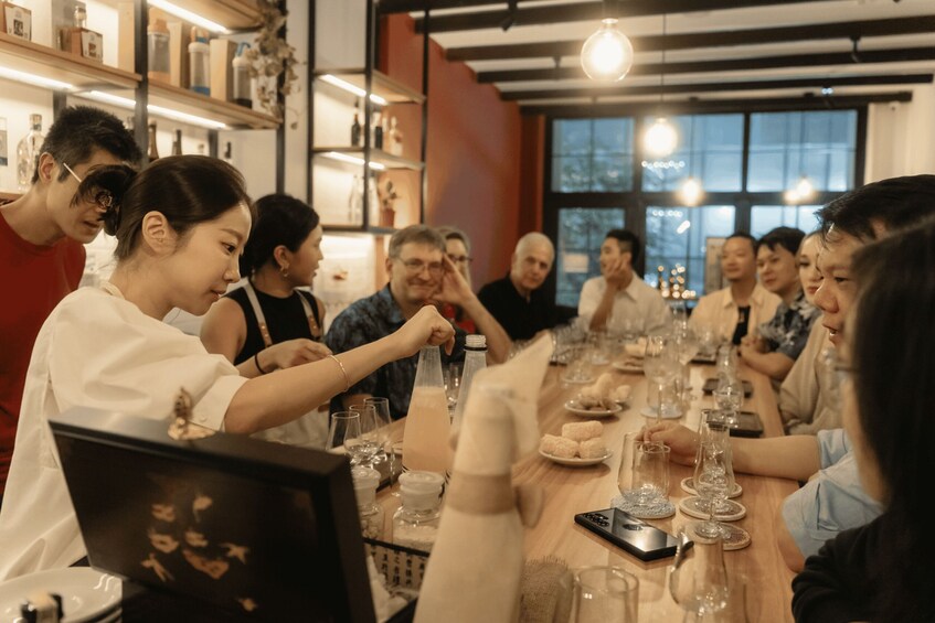 A group of people seated around a long table with various items on it, including glasses and a smartphone. 2