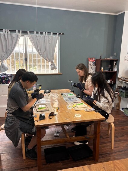 Three people working at a wooden table with papers and tools. 5