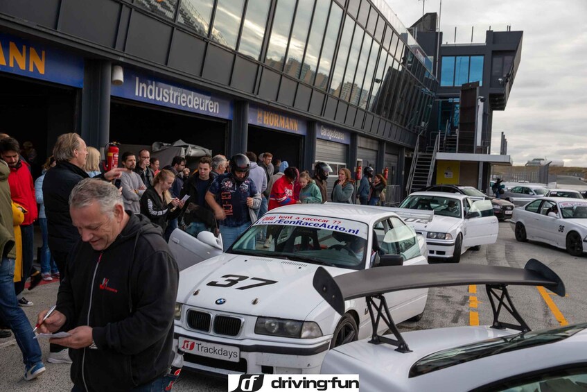 Una multitud de personas cerca de un edificio con los rótulos 'Industriedrien' y 'HORMANN', y varios BMW blancos modificados con números de carrera. 4