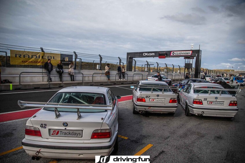 Una fila de coches de carreras en un evento de competición, con espectadores y un gran cartel de fondo. 3
