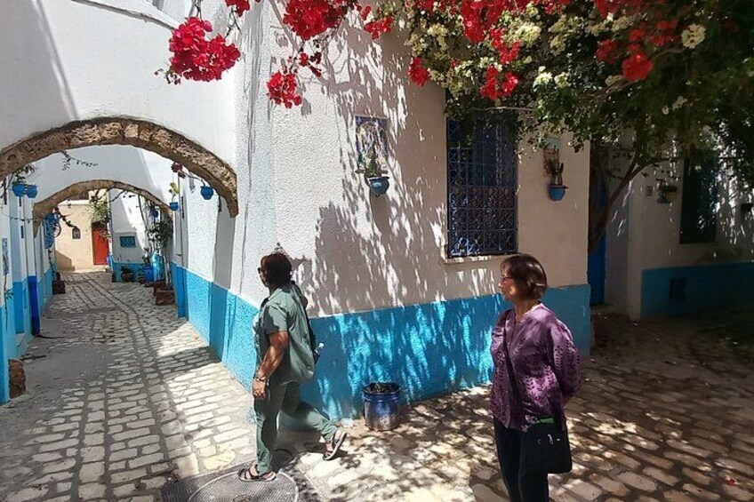 A cobblestone street with white and blue buildings, a man walking, and a woman standing. 5