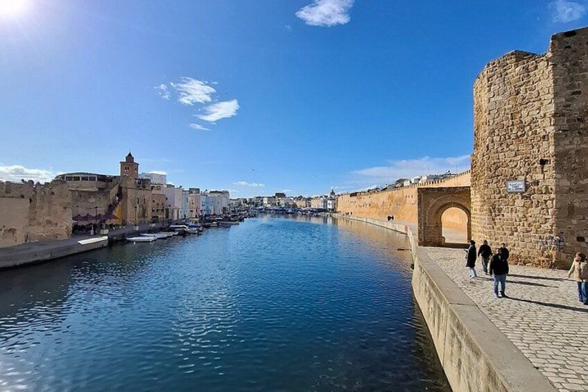 A canal with boats, a stone wall, and a tower. 4