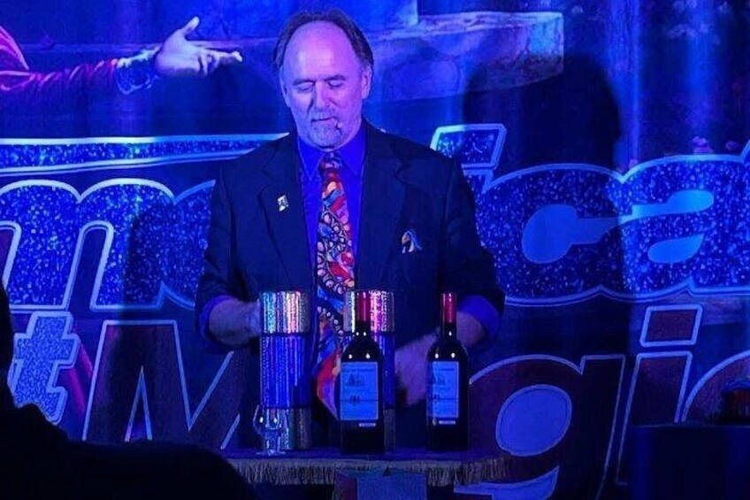 A man in a suit with a colorful tie standing at a table with two bottles of wine. 5