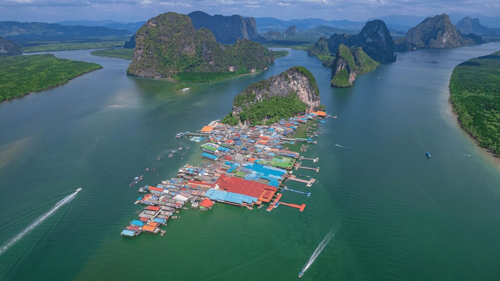 An aerial view of a floating village with numerous boats and buildings on stilts over calm waters, surrounded by lush greenery and limestone karsts. 2
