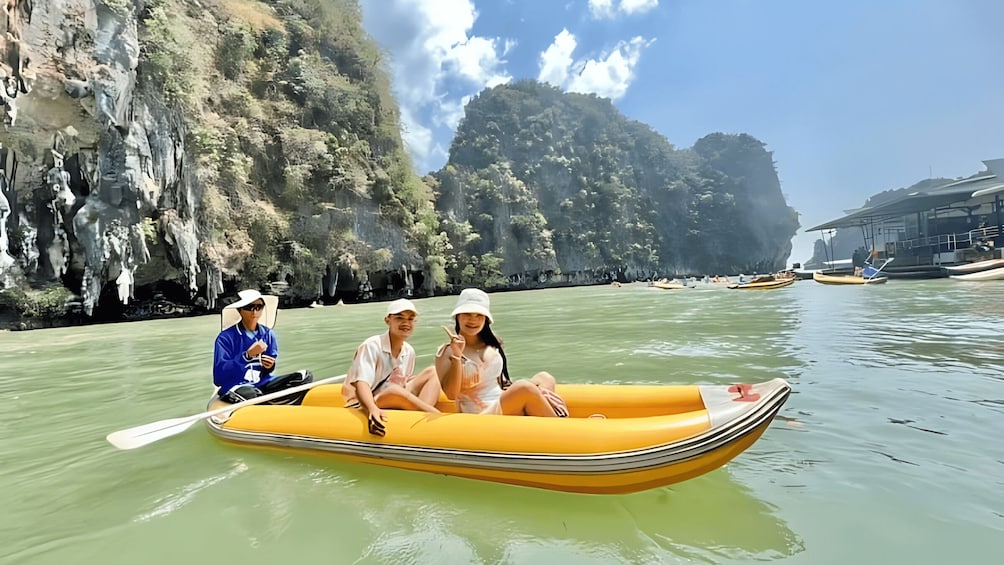 A group of people in a yellow inflatable boat on calm water, with rocky cliffs and a clear sky in the background. 3