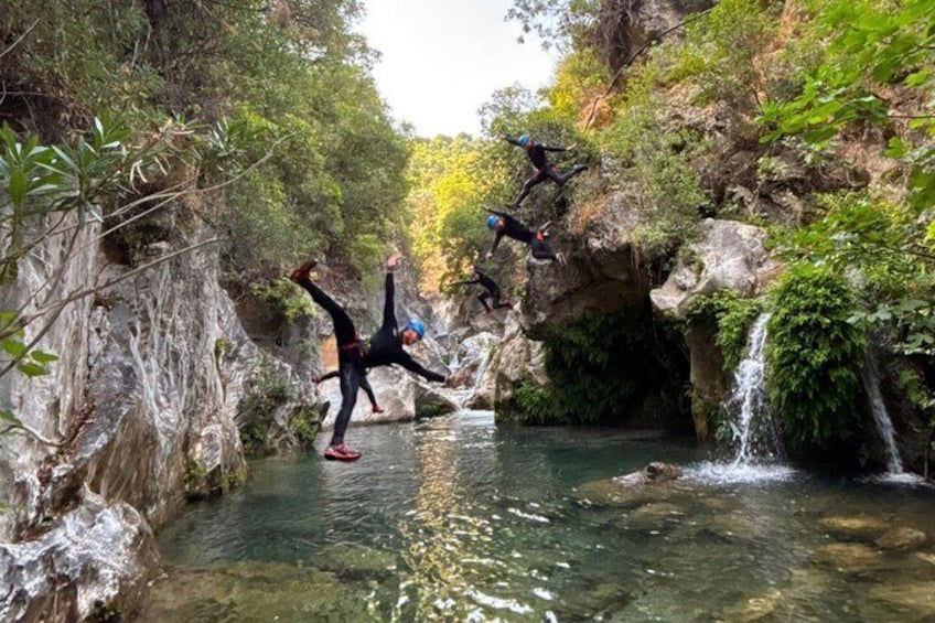 People jumping off a cliff into a river surrounded by rocky cliffs and greenery. 3