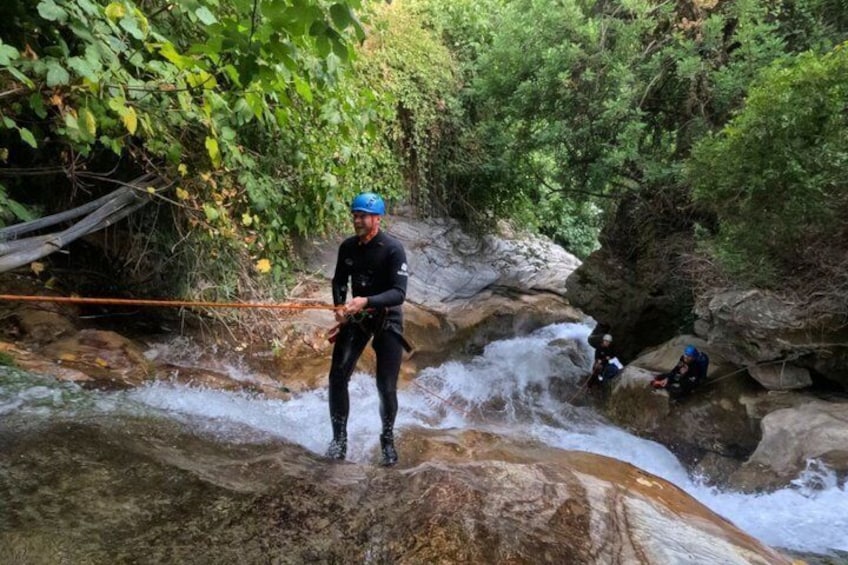 A person rappelling down a rocky waterfall in a forested area. 2
