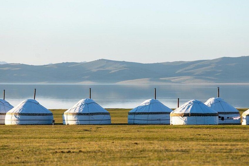 Una hilera de yurtas blancas en un campo de hierba, con un lago y montañas al fondo. 3