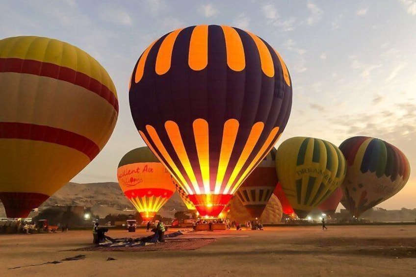 A group of hot air balloons on the ground with a mountainous backdrop. 2