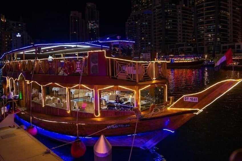 A boat with illuminated railings and a flag, docked at night with city buildings in the background. 1