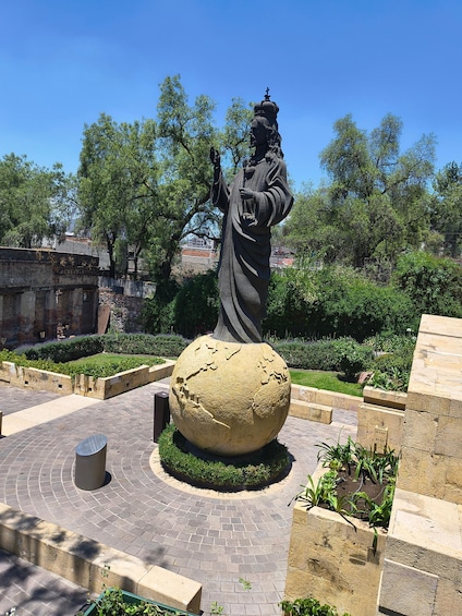 A statue in a garden with a large spherical stone and brick pathways. 5